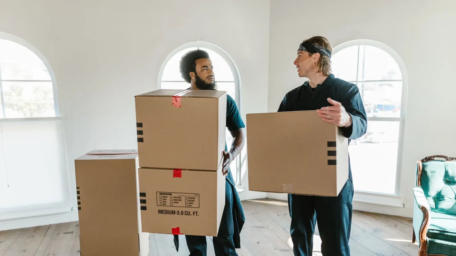 Two movers carrying labelled cardboard boxes through an empty room, illustrating Google Ads cost per lead for home service companies